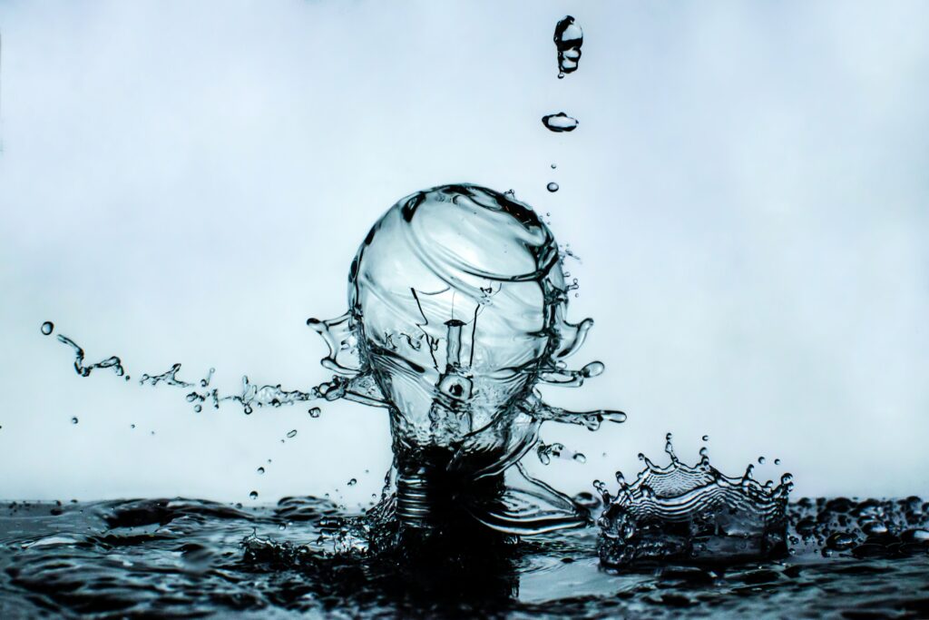 A light bulb appears to be splashing out of turbulent water, with water drops surrounding it