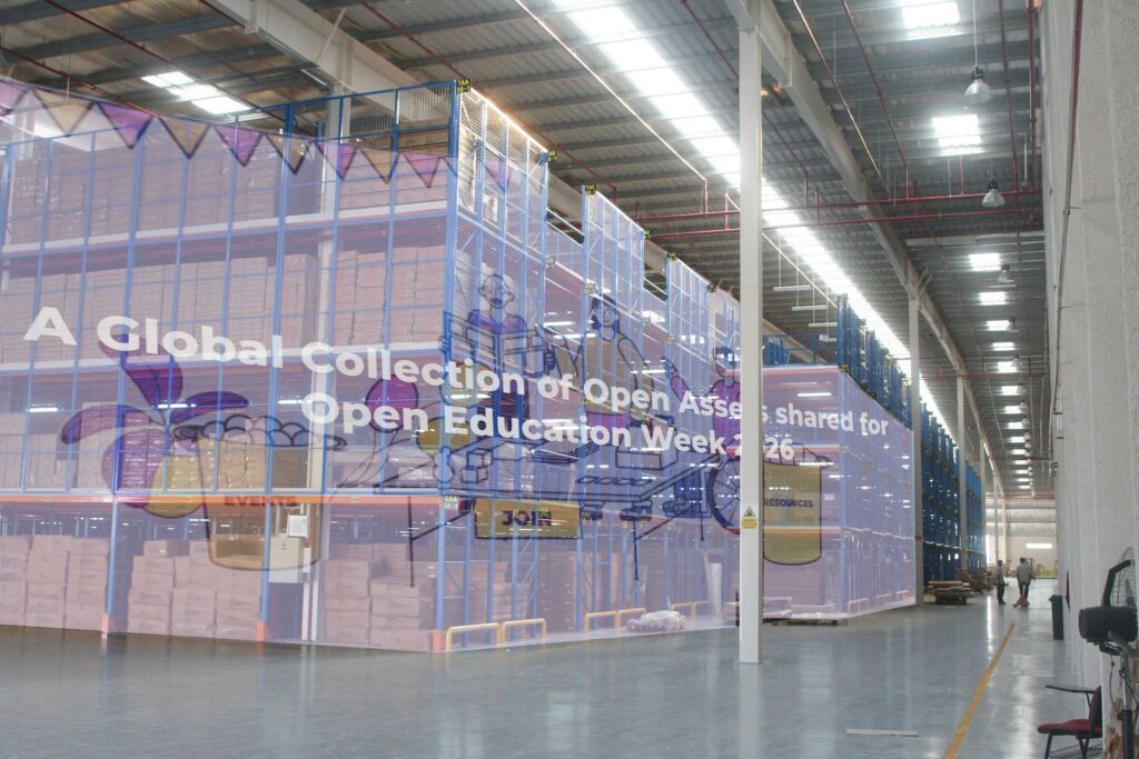 A large warehouse with superimposed on the shelves the OEWeek banner for Sharing Open Assets in 2026.
